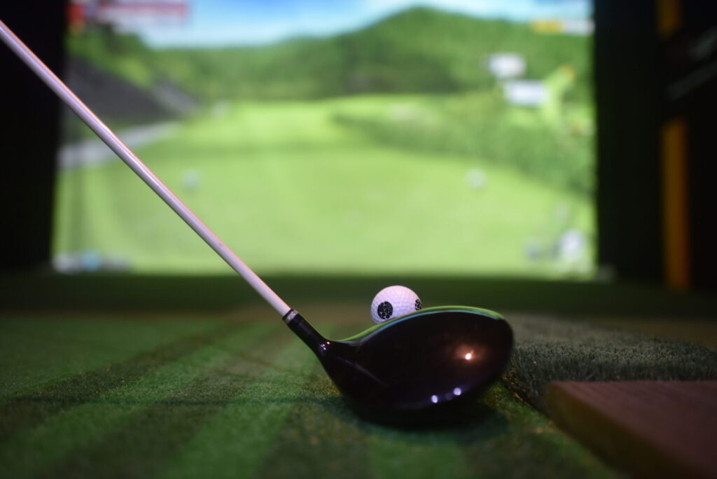 屋内シュミレーションゴルフで、セットされたゴルフボールとドライバーの画像