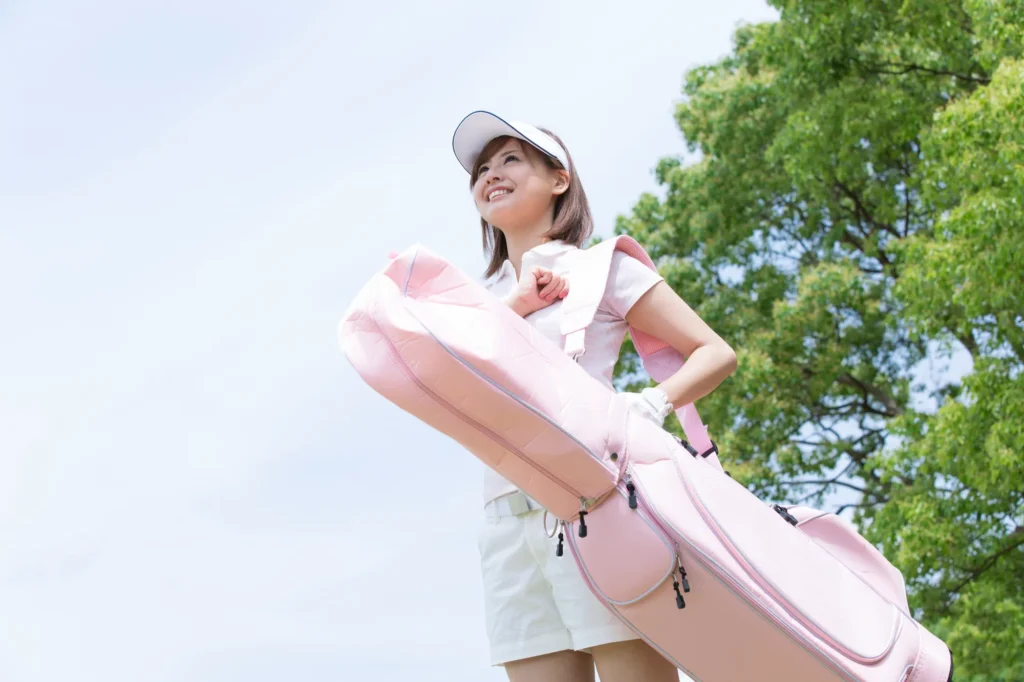 ピンクのゴルフバッグを持って微笑む女性