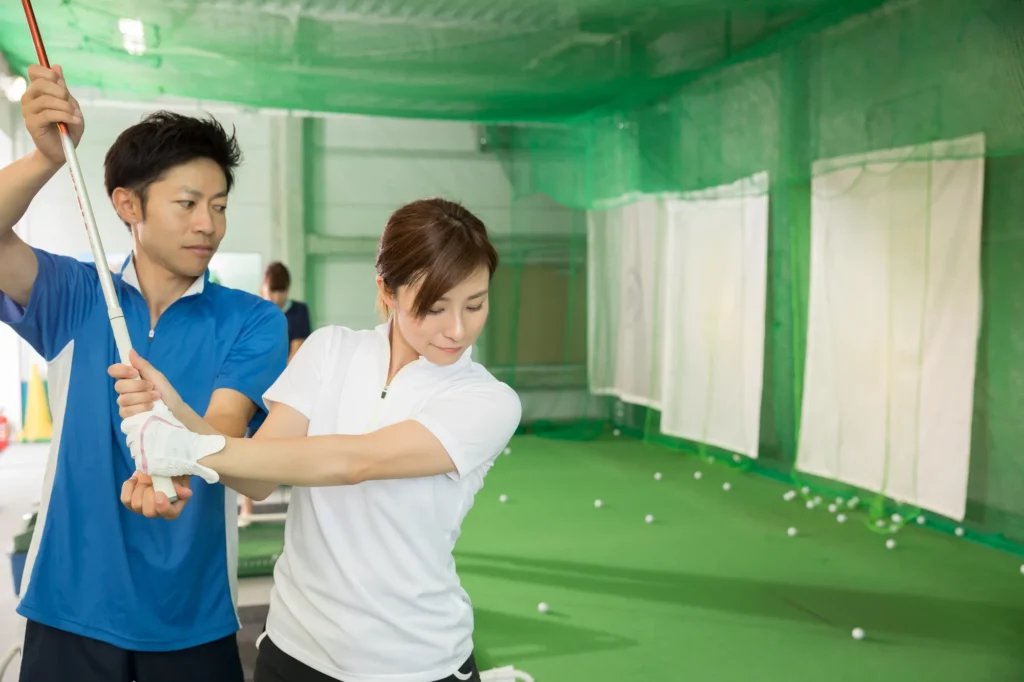 室内練習場で女性に指導する男性ゴルフコーチ