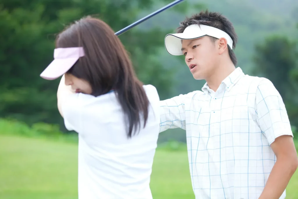 屋外練習場で女性に指導する男性ゴルフコーチ