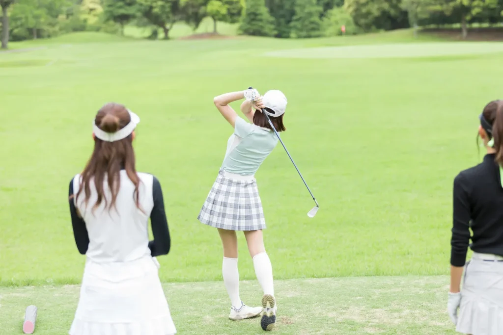 ショットを打つ女性ゴルファーとそれを見守る2人の女性ゴルファー