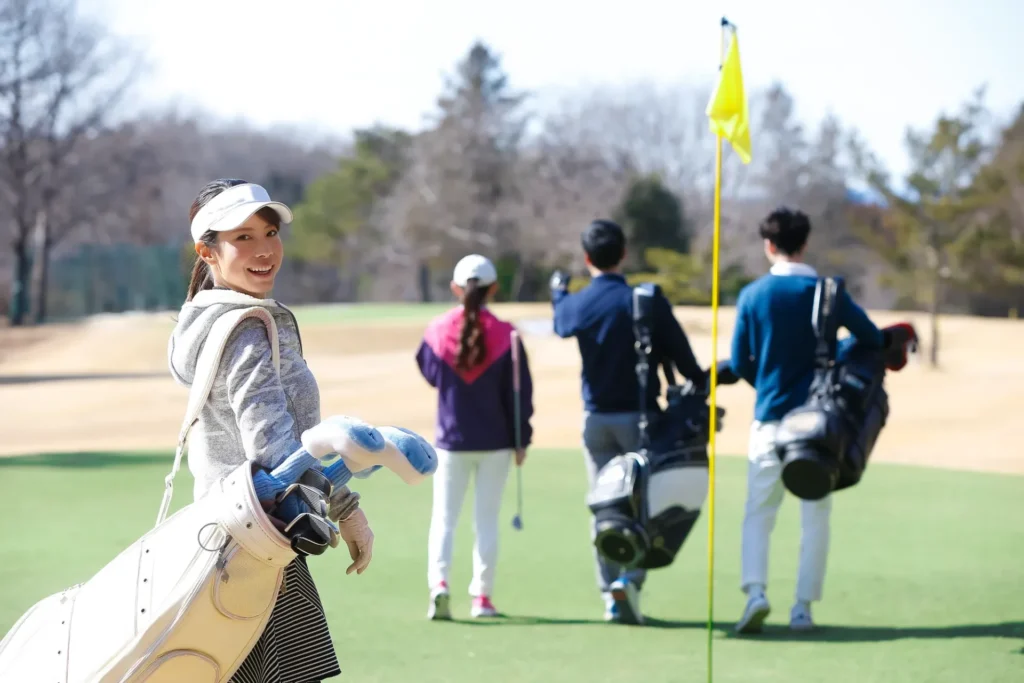 ゴルフバッグを持ちながら振り返る女性ゴルファーと3人のゴルファーの後ろ姿